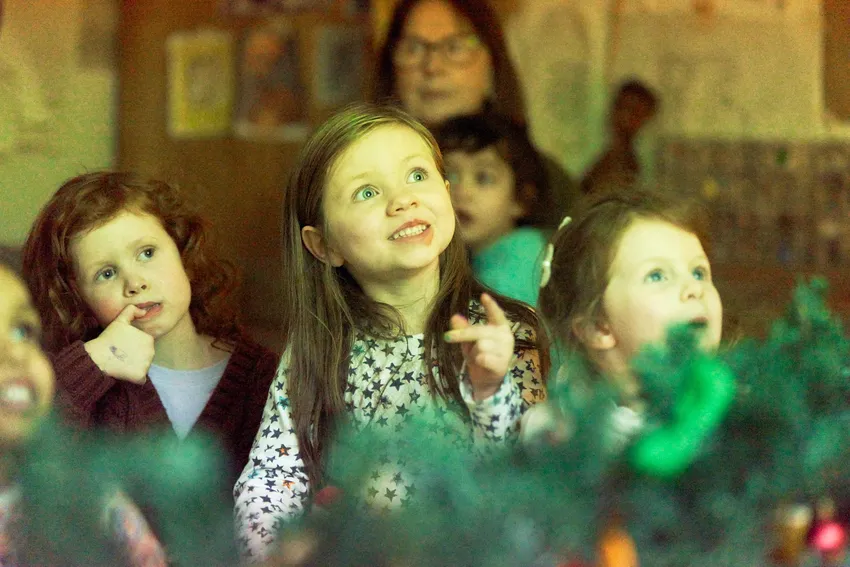 Child smiling at something offscreen, with out of focus festive decoration across the bottom of the image.