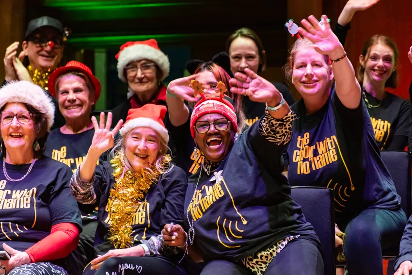 CWNN London choir member in christmas decorations smiling and waving on stage at a christmas gig