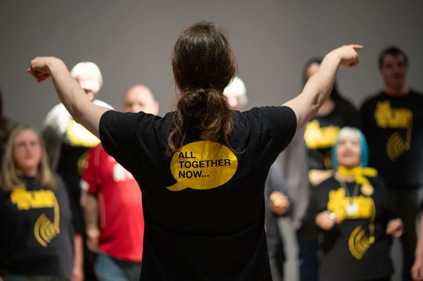 CWNN Choir director conducting a choir in t shirt saying All Together Now