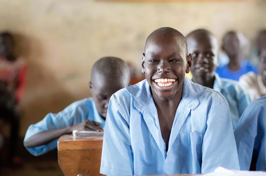 Boy in a blue shirt, sitting at a school table, smiling.
