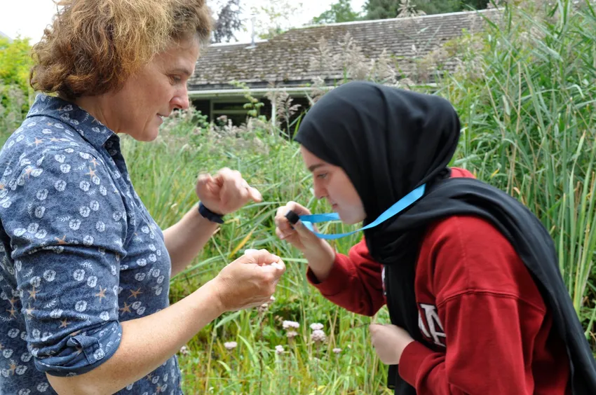 Young person with headscarf examining a leaf with a tutor