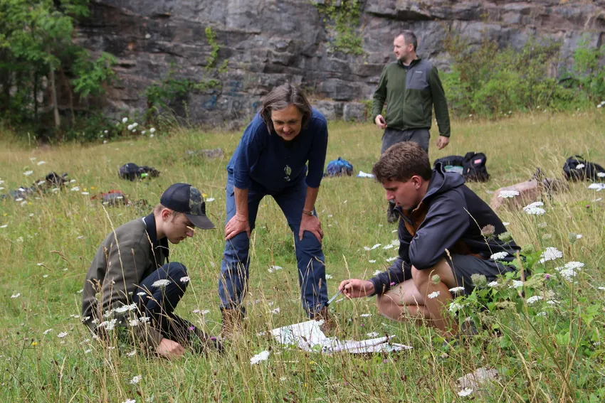 Two young people, assisted by tutor, conducting fieldwork in a meadow by a cliff