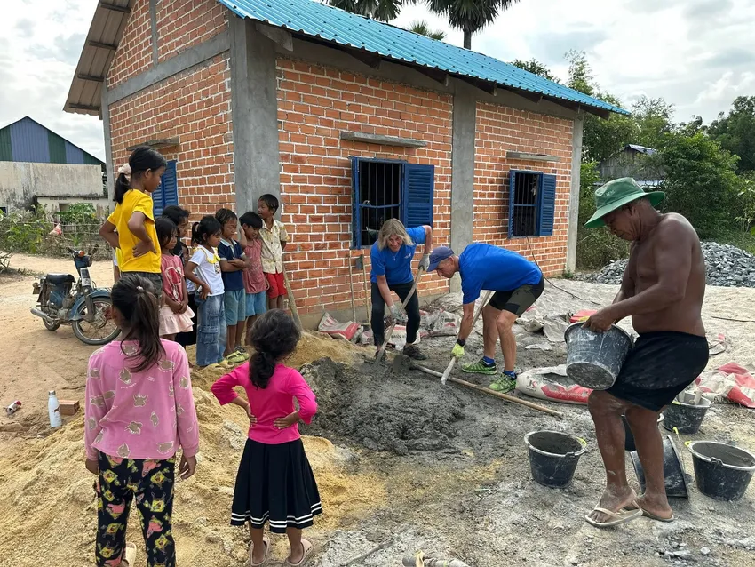 Chris in Cambodia mixing cement while the children who will learn in the new school watch on.
