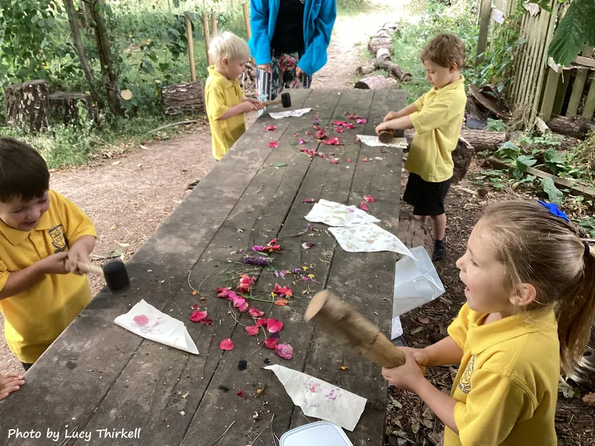 Children using wooden mallets to print colourful flowers and leaves onto fabric during a hands-on outdoor learning activity.