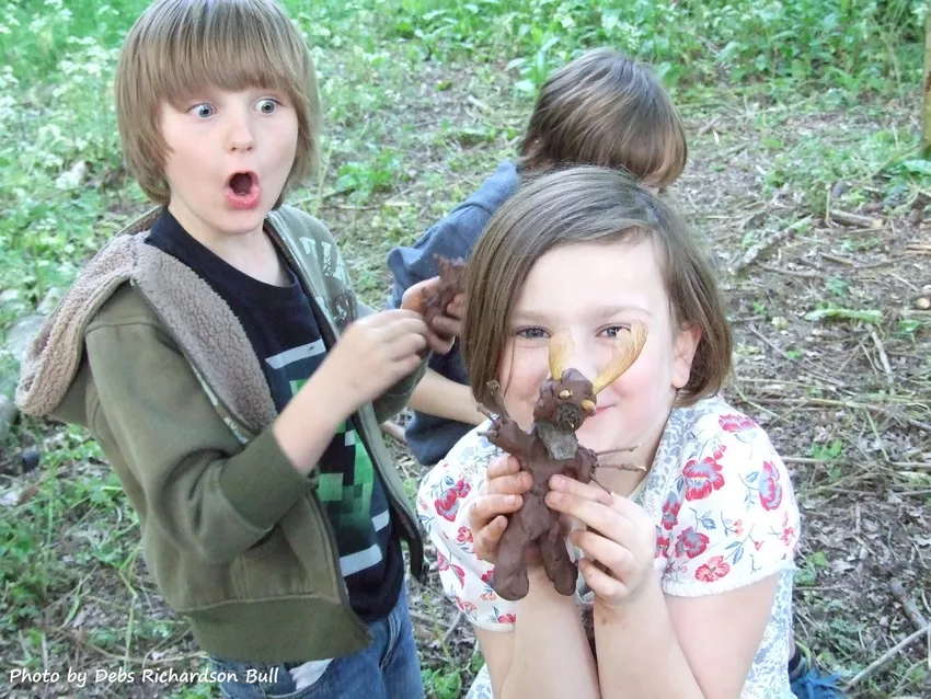 Children taking part in an outdoor learning activity, holding up a creative woodland creature made from mud, sticks, leaves and seed pods.