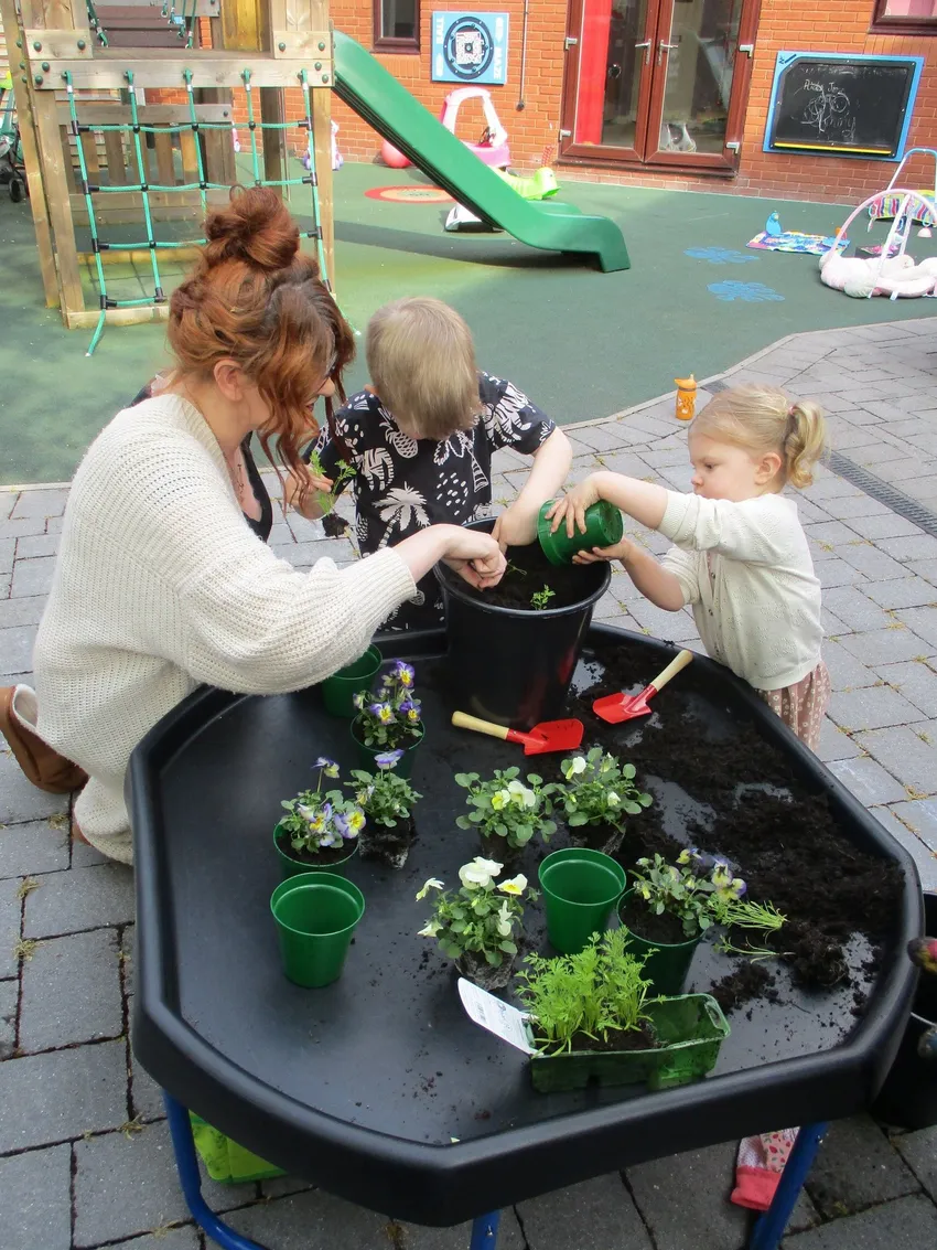 Mum and children playing happily planting plants outside in a play area