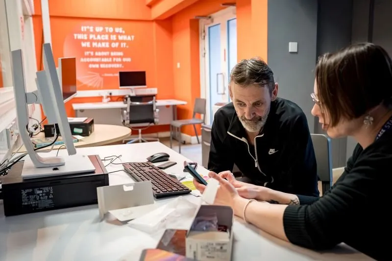 A resident and a support worker in the IT suite working together to set up a new mobile phone