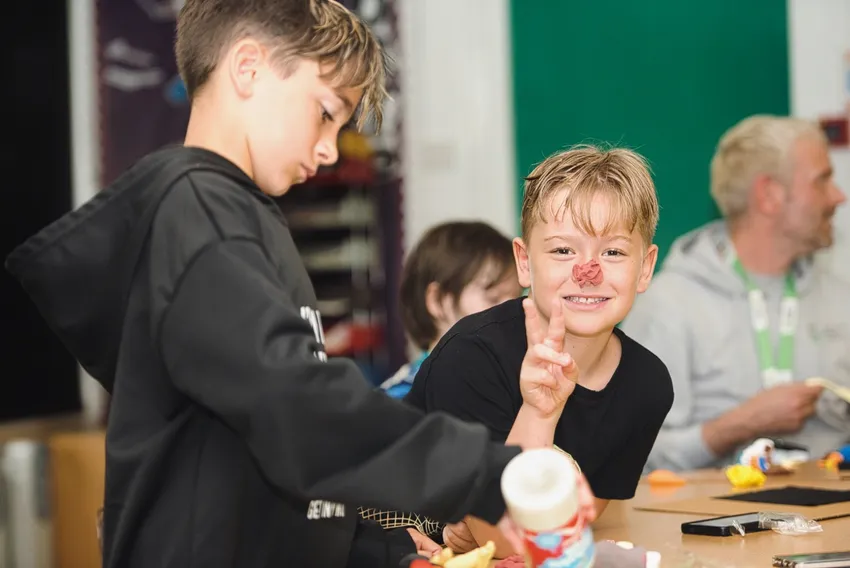 Two boys enjoy arts and crafts at our HDYES summer camp. One has made a clown's nose from plasticine and is smiling at the camera.