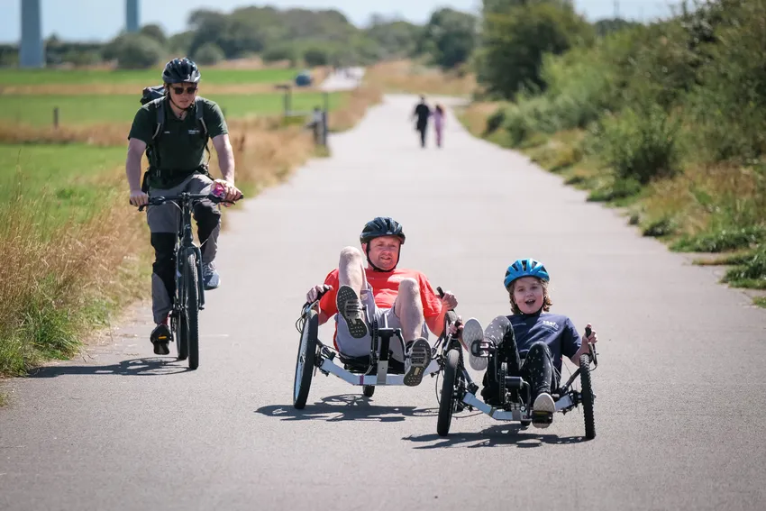 Man and young girl cycling inclusive KMX bikes on a wide open surface with an instructor just behind on a two-wheeled bike