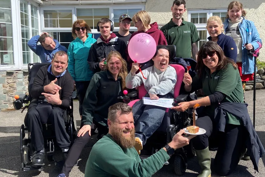 Group of mixed ability guests and instructors celebrating the 20th visit of Francesca, who has CP, with balloons and cake