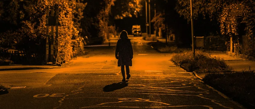 A woman walks alone at night on a deserted street.