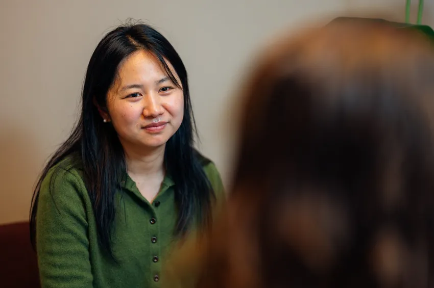 a woman wearing a green cardigan is smiling encouragingly, listening to a woman who has their back to the camera.