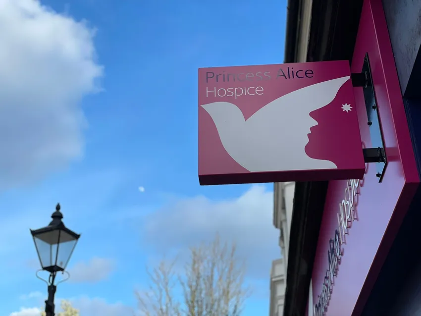 A pink Princess Alice Hospice shop sign displaying the charity's logo, mounted on the side of a building.