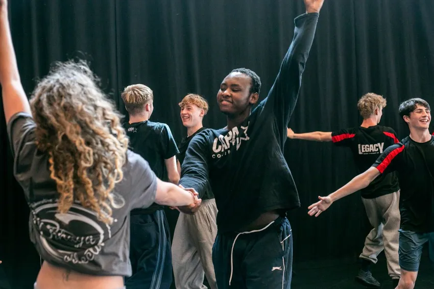 Young people dancing together with outstretched arms at the Bhangra Ceilidh, delivered by EFDSS at U.Dance National Festival 2025. Image credit Dani Bower for One Dance UK