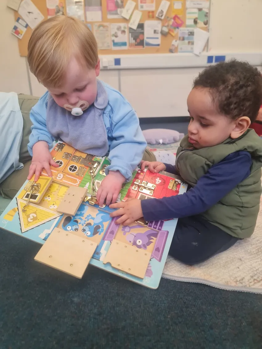 Two young children playing with a latches board together at one of Home-Start Banbury, Bicester & Chipping Norton's group sessions.