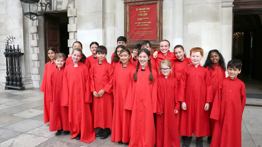 Young singers of the Junior Choir of St Martin-in-the-Fields wearing red cassocks and smiling enthusiastically in the camera.