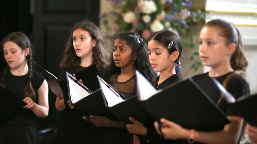 Singers from the Junior Choir at St Martin-in-the-Fields in formal black attire, holding black choral folders and singing passionately.