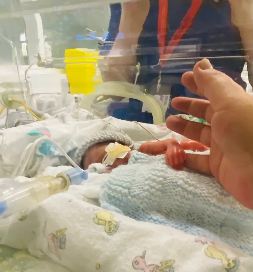 A baby inside an incubator with their parents holding their hand
