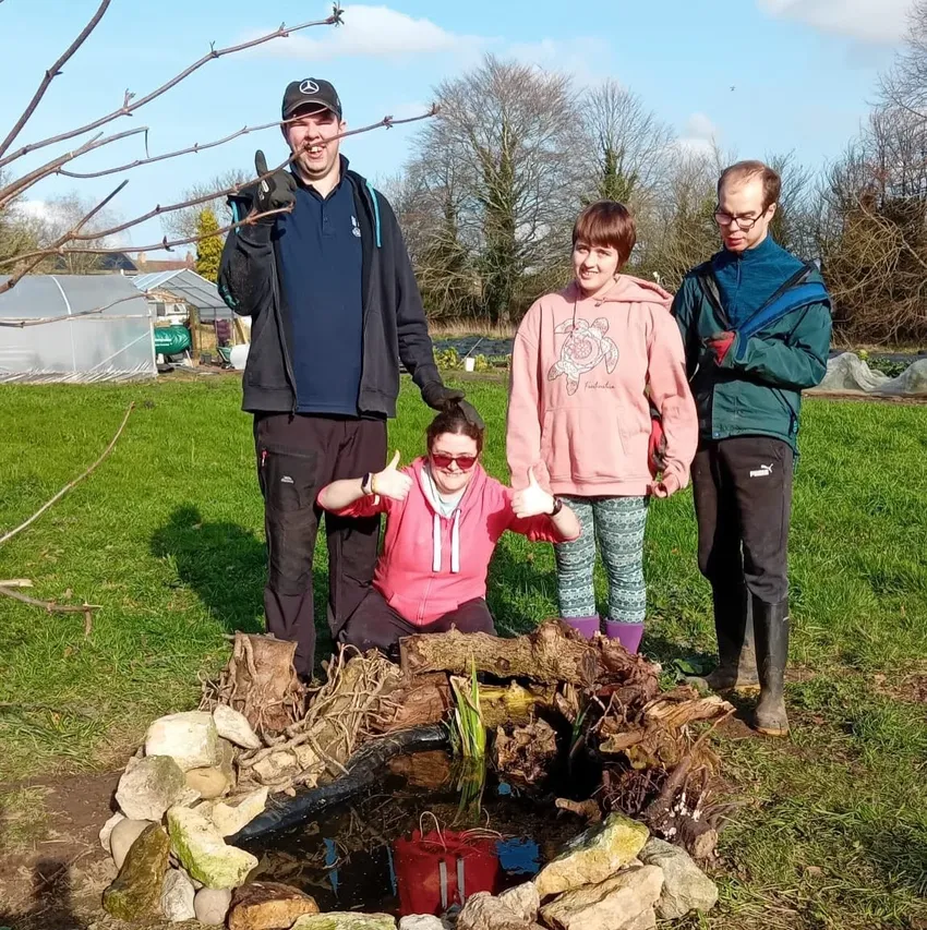 2 women and 2 men standing and crouching proudly behind a newly finished pond for wildlife