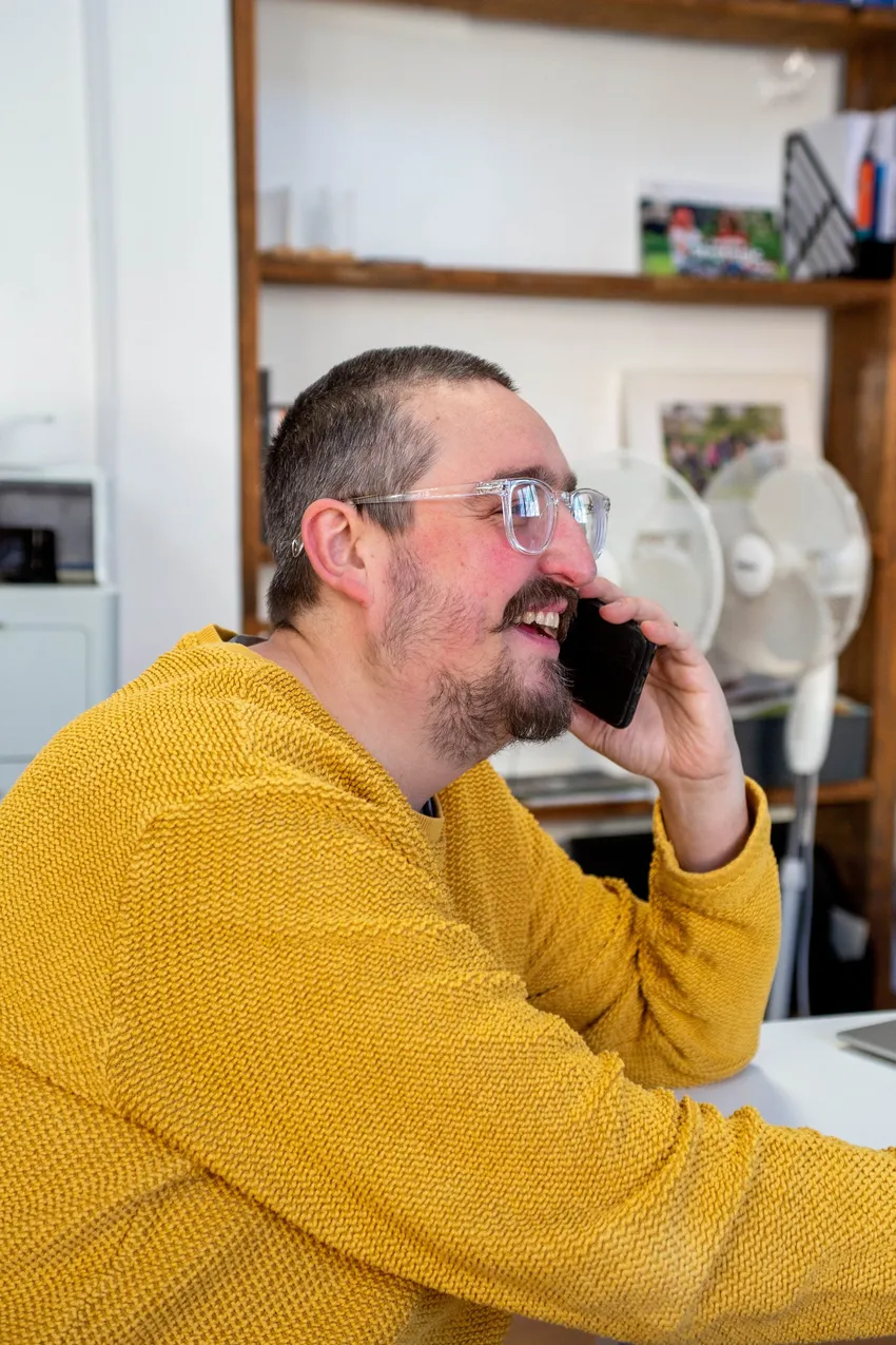 Justlife Frontline worker supporting a client over the phone at his desk, smiling.