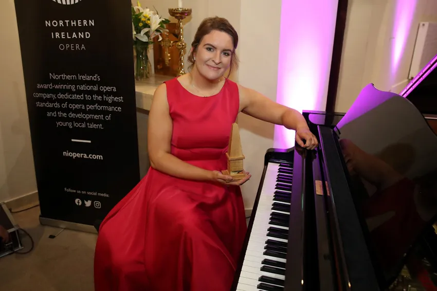 A woman in a red dress sits at a grand piano, preparing to play. This was part of a weekend artist development programme on the North Coast of NI, which involved training and public performance for emerging singers and a pianist.