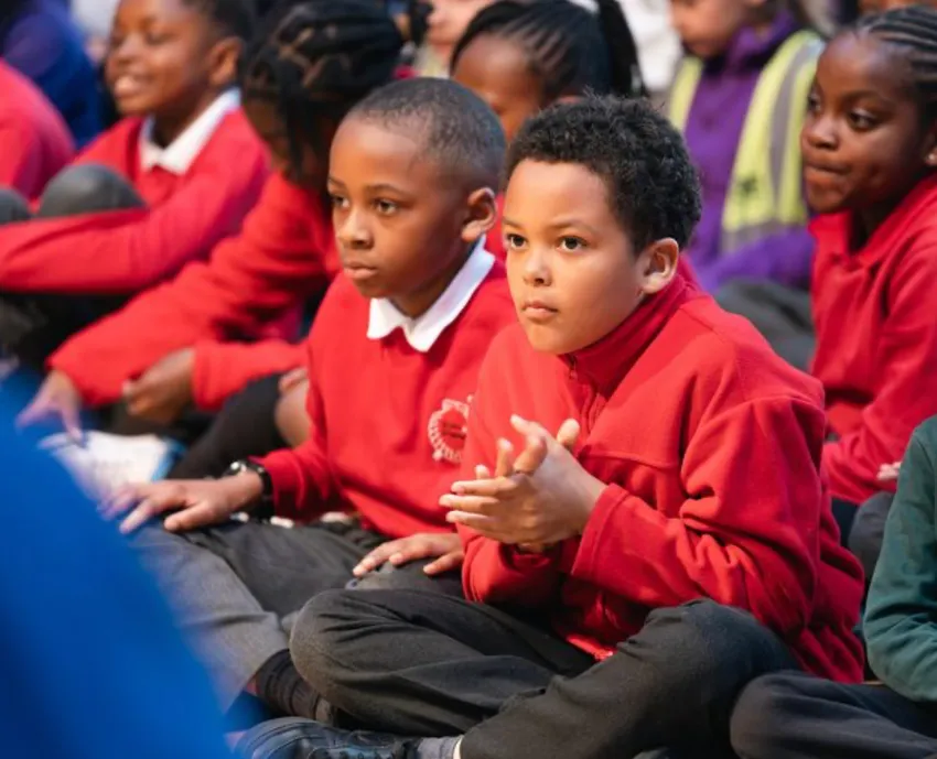 Young children seated on the floor and leaning forward listening.