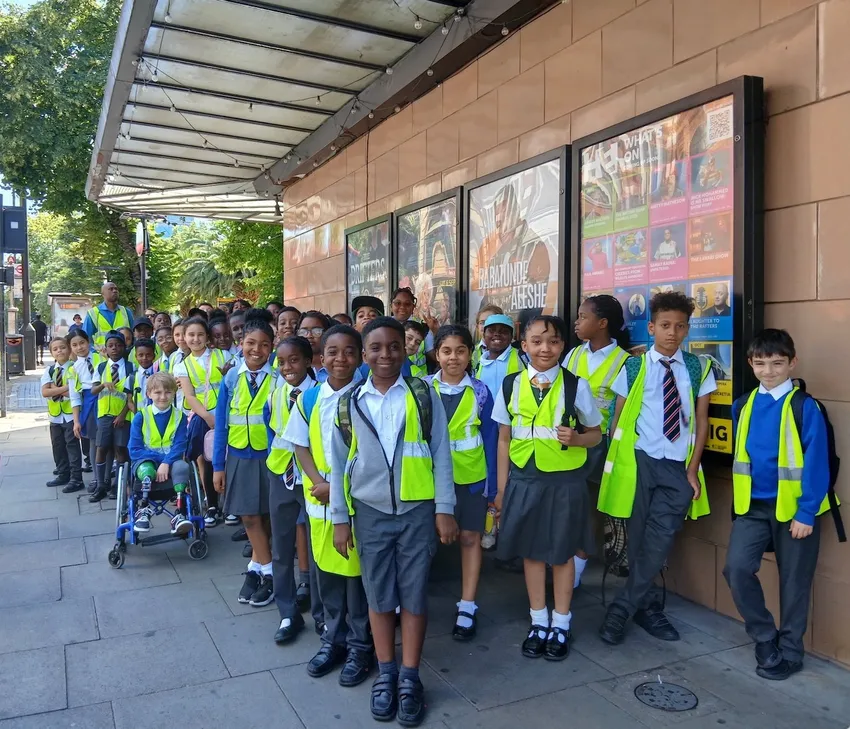 Children smiling and looking at the camera, waiting outside a theatre