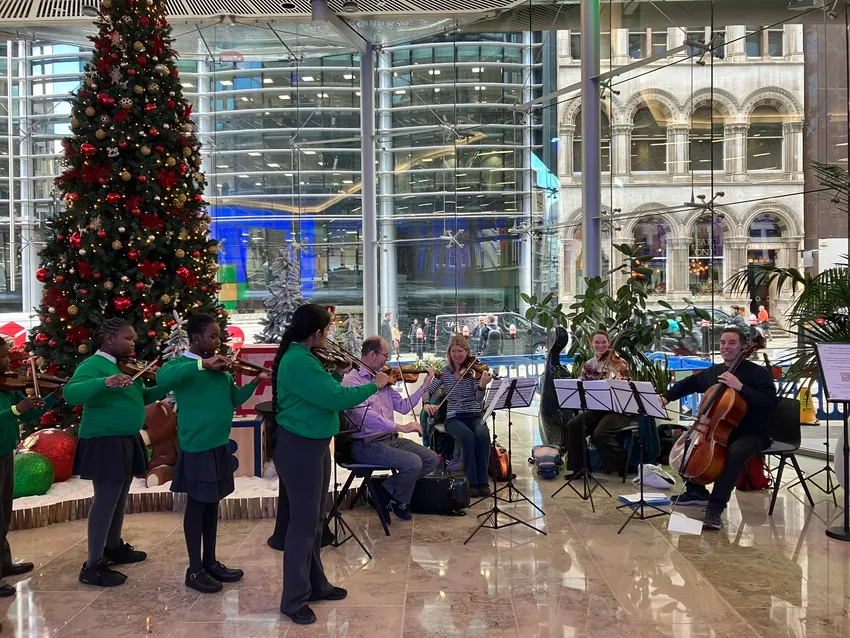 three children play violin in front of a Christmas tree