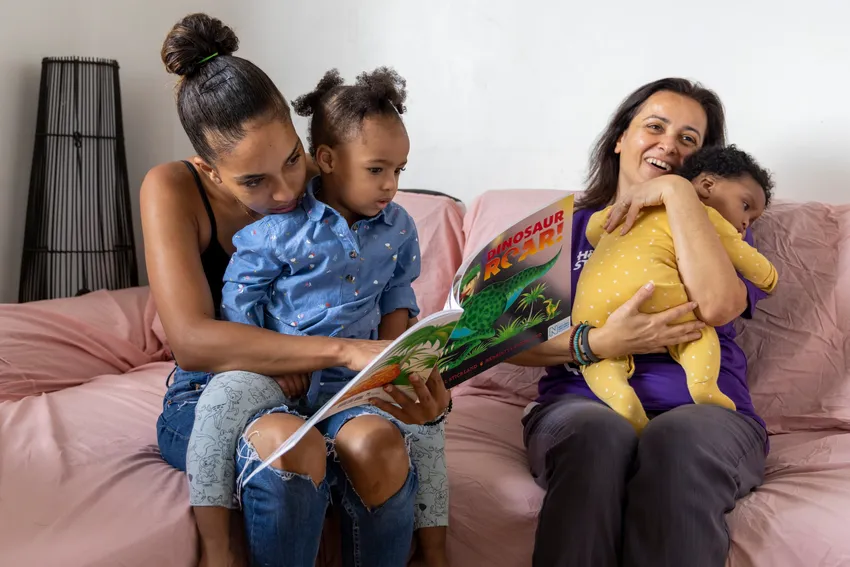 Mum and toddler reading while volunteer holds baby