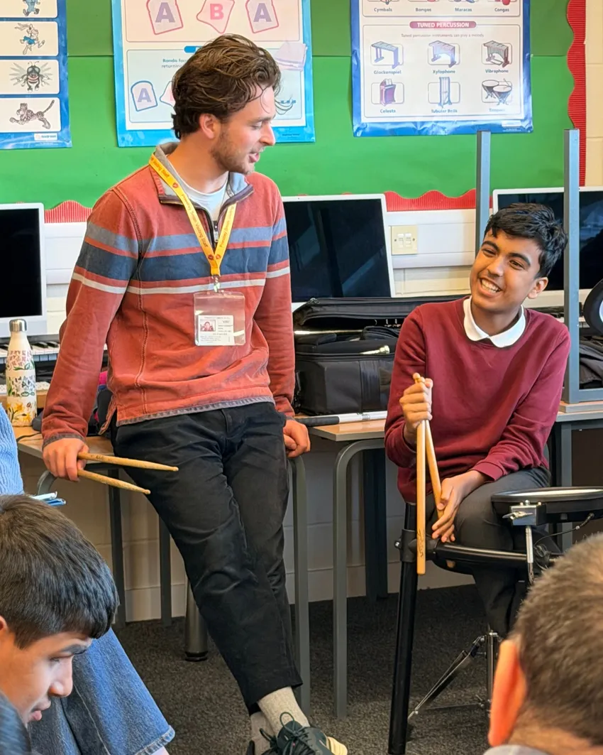 A Swan musician and a young child, both holding drumsticks, are smiling at one another.