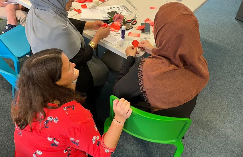 Refugee women being supported by a volunteer to complete a craft.