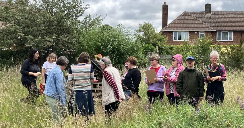 A group of ten people stand together in tall grass. 2 are holding clipboards as they gather around at Flower Pod Newark.