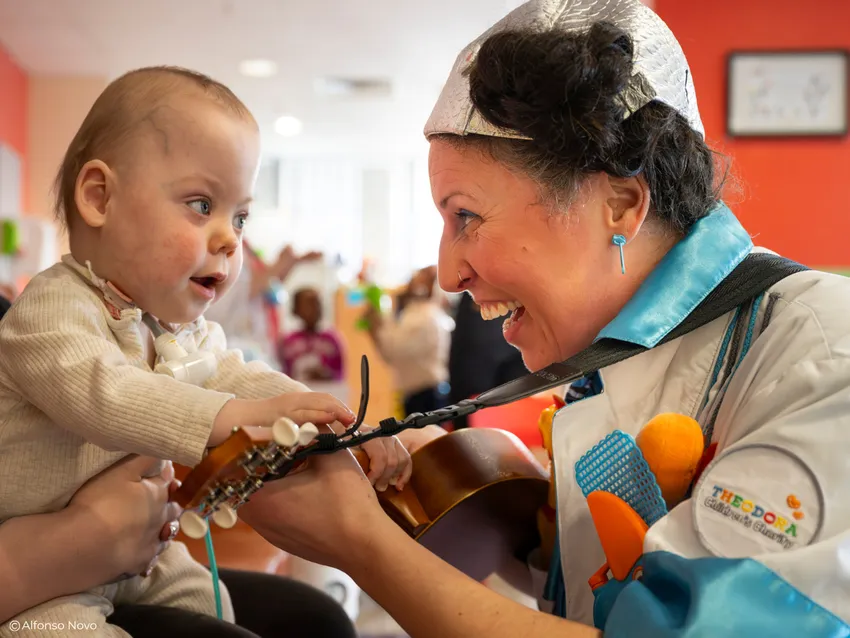 Dr Nic Nac is playing ukulele for a baby, they are making eye contact and smiling at each other in a moment of connection.