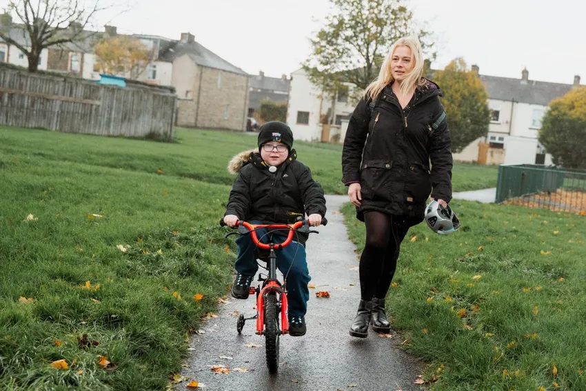 Boy riding his bike with his mum walking next to him.