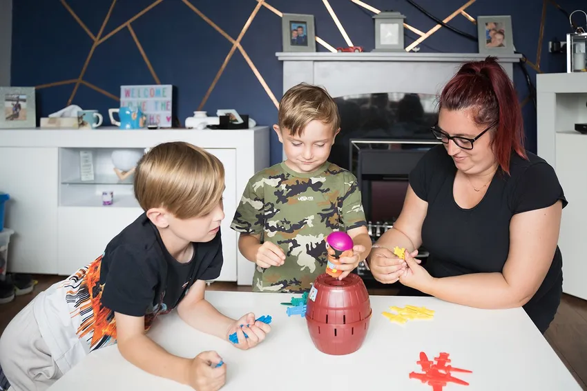Two boys playing a game on a table with a lady.