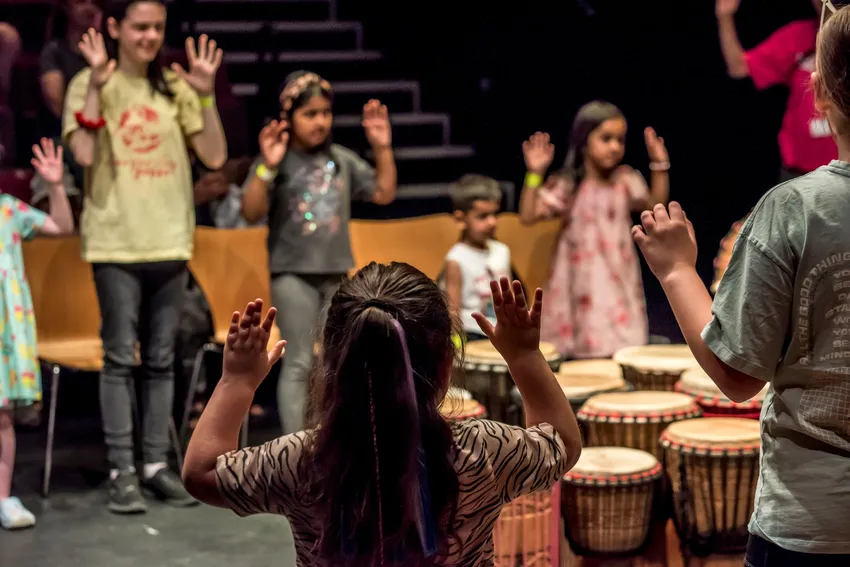 A group of children with hands up taking part in a performance with drums