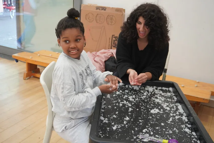 A volunteer engages a KEEN London athlete with sensory snow making, they both smile as their hands experience the strange texture