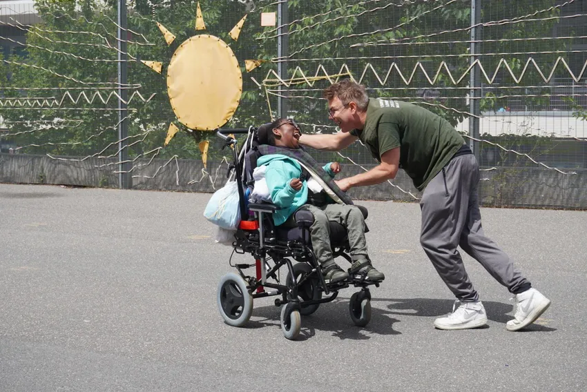A KEEN London volunteer dances in the playground with one of our athletes who is smiling in his wheelchair making eye contact as they engage