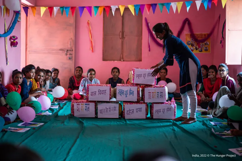 A young woman leading a group session with adolescent girls in India, with boxes labelled in Hindi representing barriers girls face.