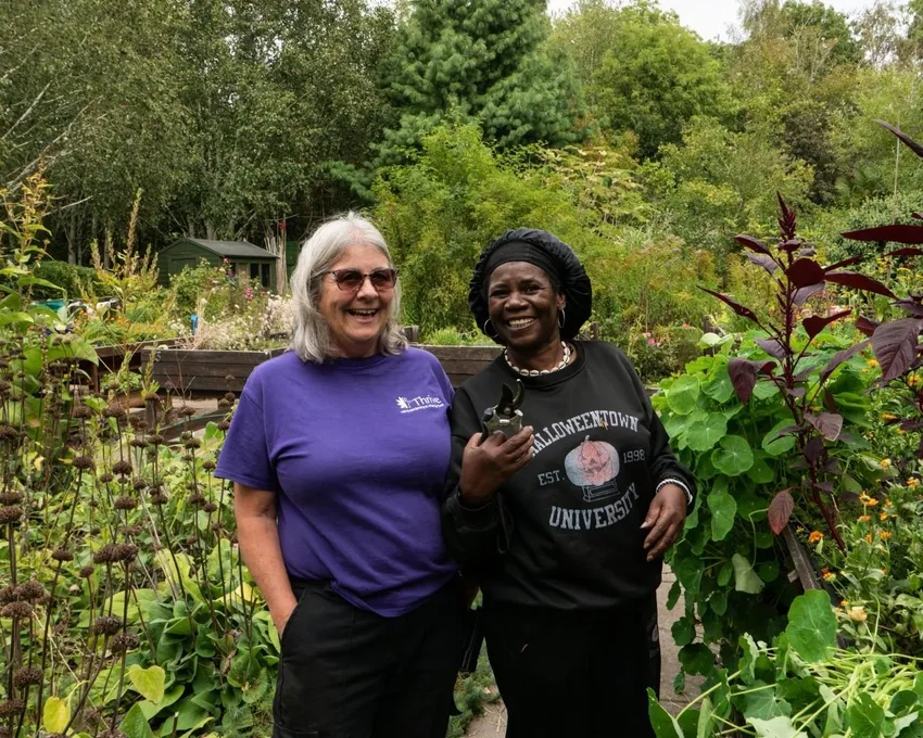 Thrive practitioner, Sharon, stands with Client Gardener, Ciceley, in the garden surrounded by plants.