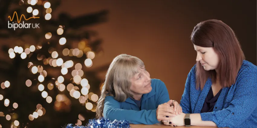 Christmas tree with warm lights and two women sitting at a table holding hands.