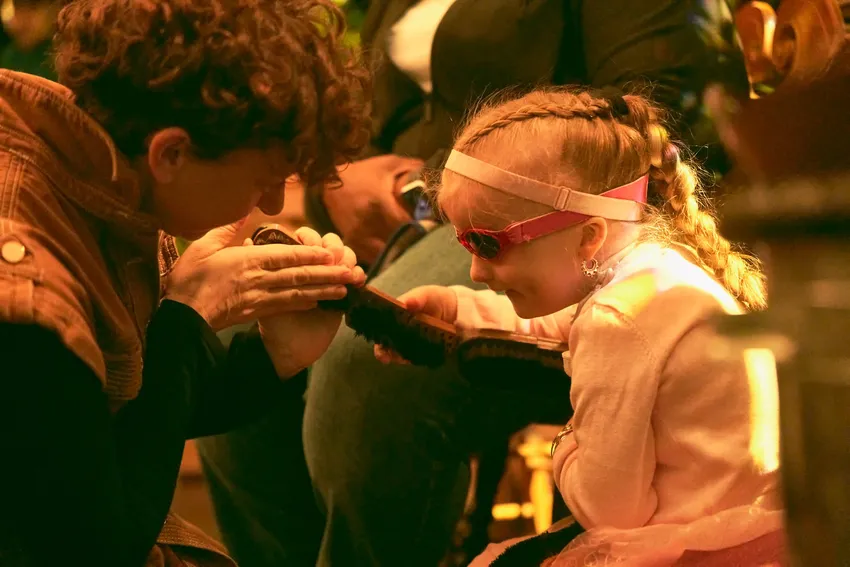 An actor is showing a child a caterpillar puppet made from brushes, which they are both holding,