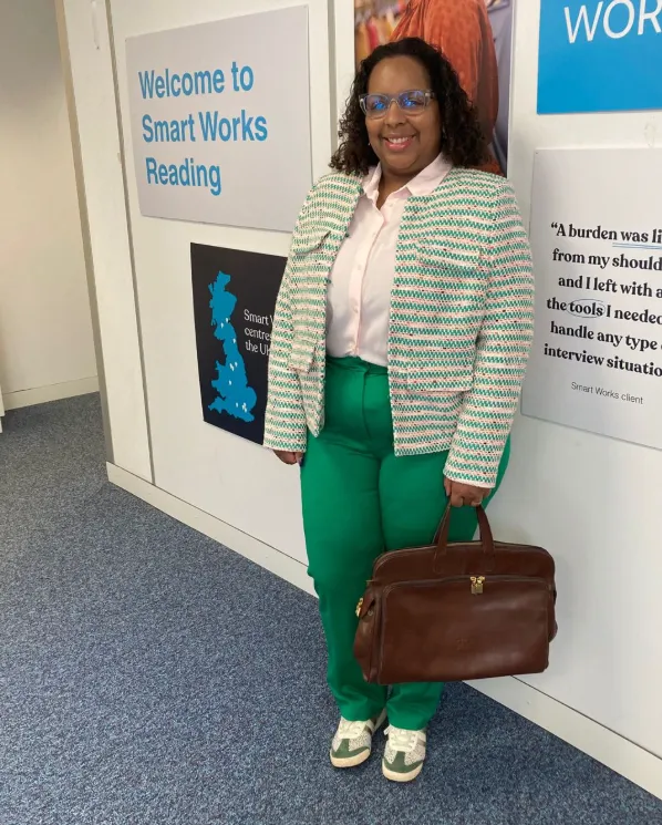 Smart Works Reading Client Tatiana stands next to the Smart Works Reading sign in her interview outfit provided by Smart Works Reading.