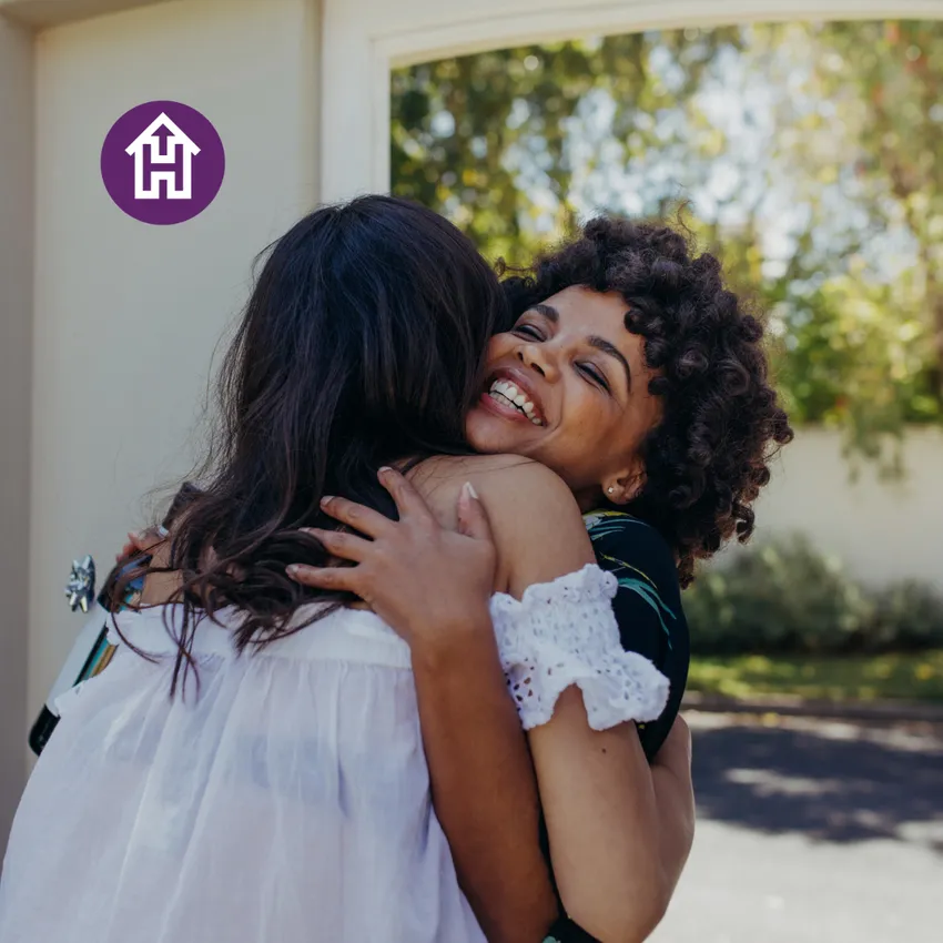 A smiling woman hugs another woman, reflecting welcome and connection