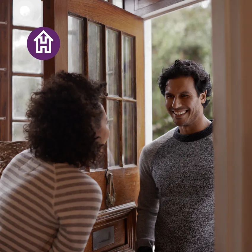 A woman opening a door to a smiling man, symbolising a warm welcome and a safe place to stay