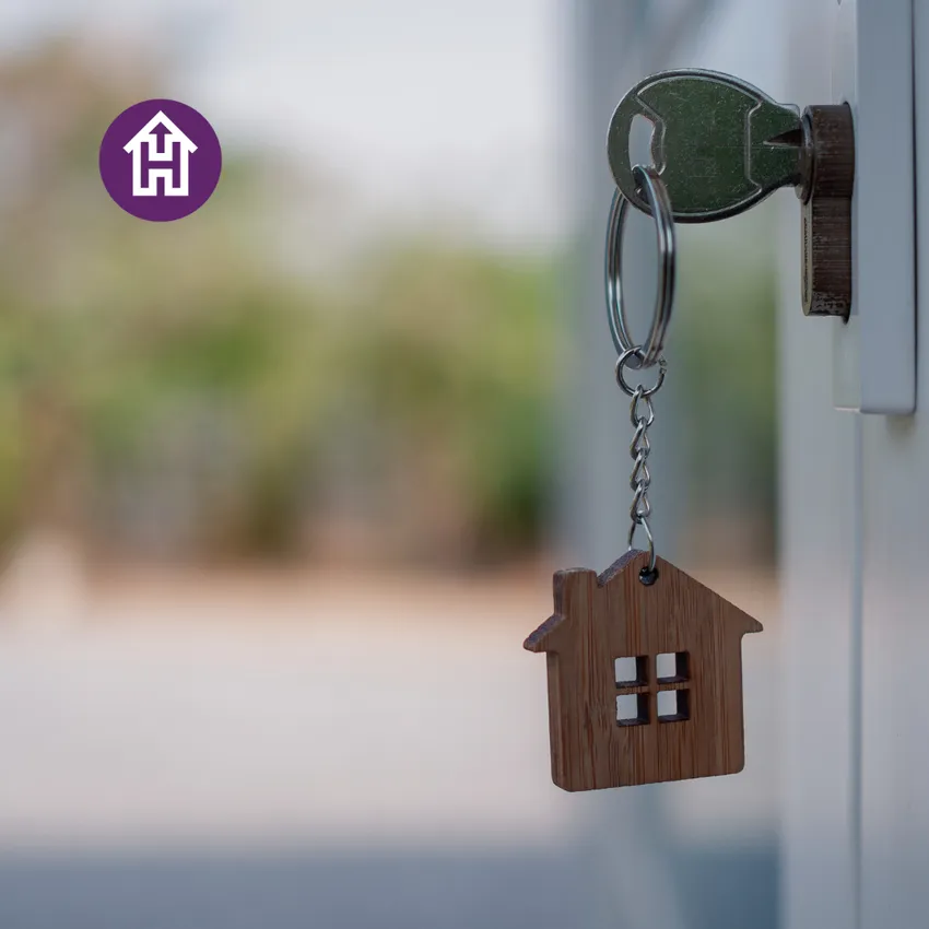 A key inserted into a lock with a house-shaped keyring, representing security and stability