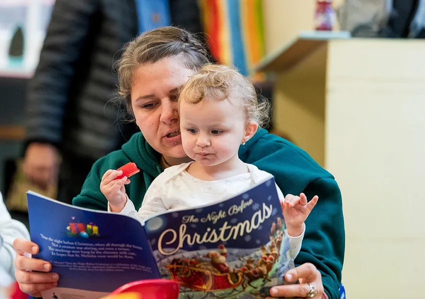 Mum reads a Christmas book to their toddler at a stay and play group