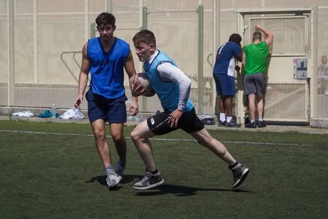 A rugby player in a light blue bib sprints with the ball