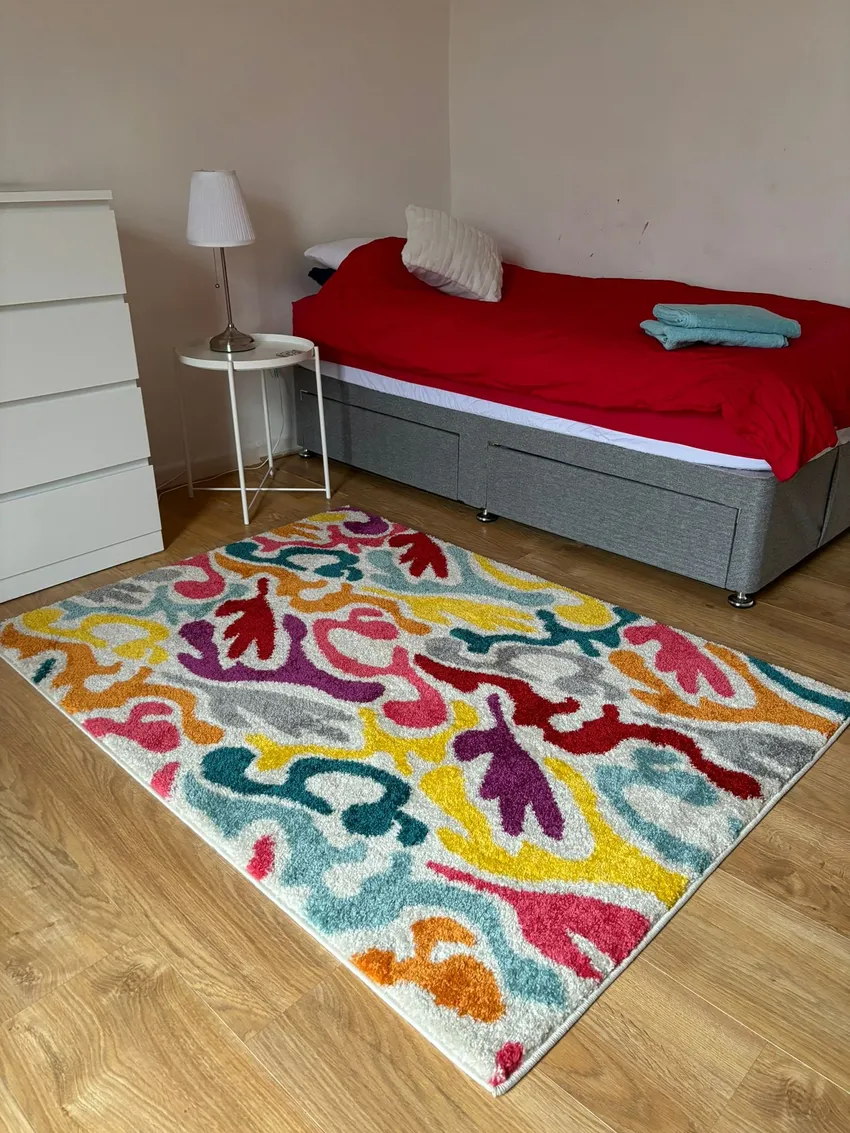 Example refuge room for single person, showing single bed, bedside table and lamp, chest of drawers and rug.