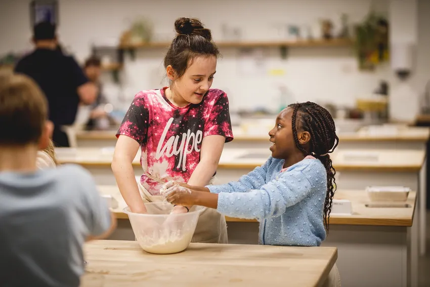 two young girls with hands in a bowl of flour